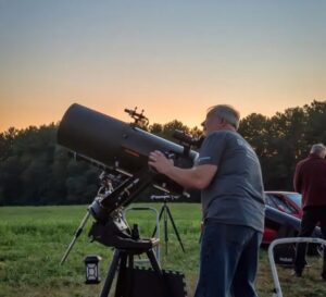 A man looking through a telescope in a field.