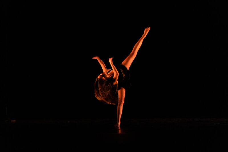 A dancer is performing on a dark stage.
