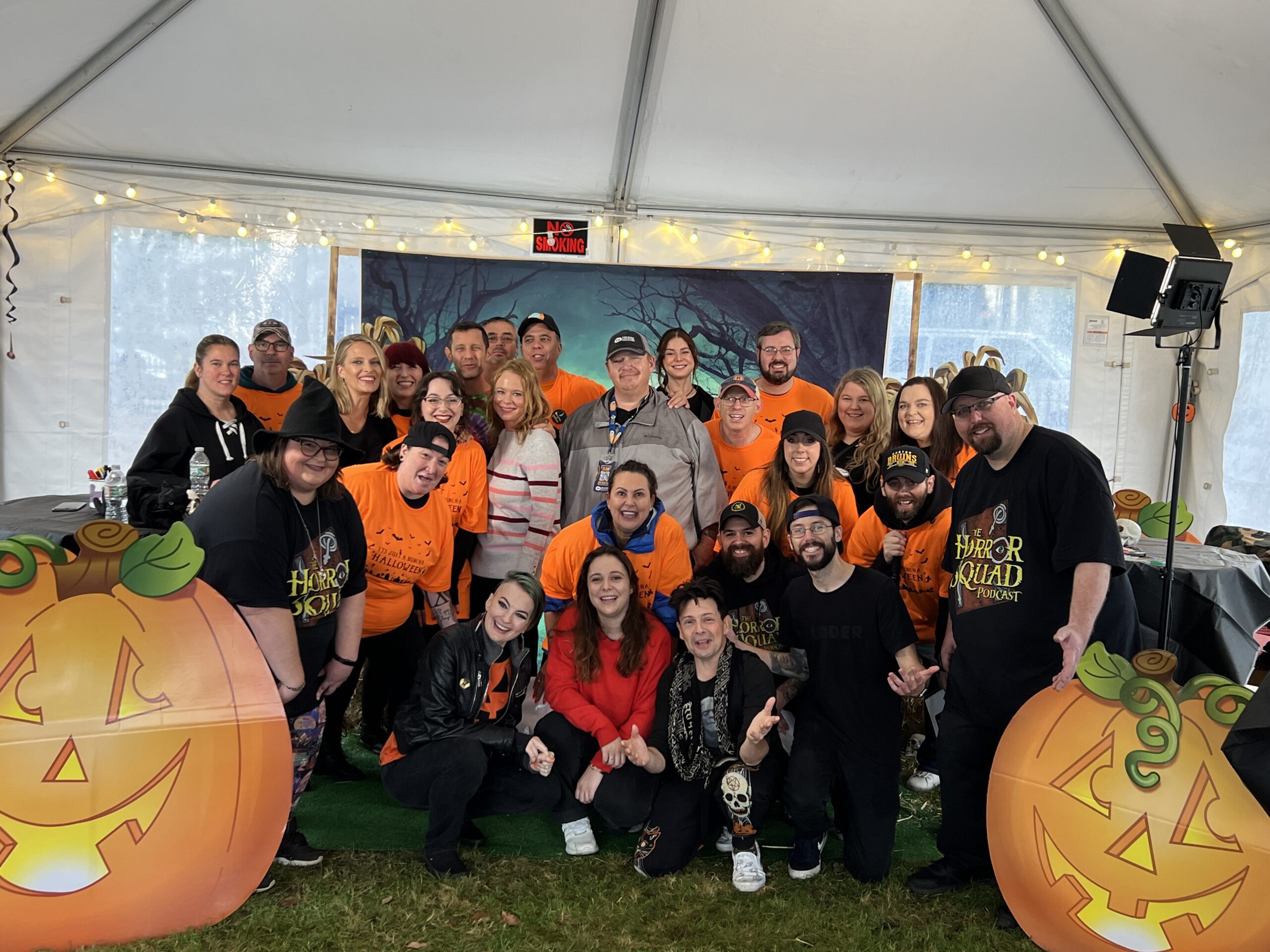 A group of people posing in front of a tent with pumpkins.
