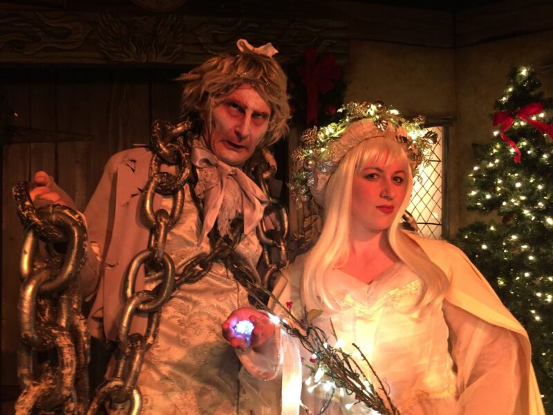 A man and woman dressed up in costumes in front of a christmas tree.