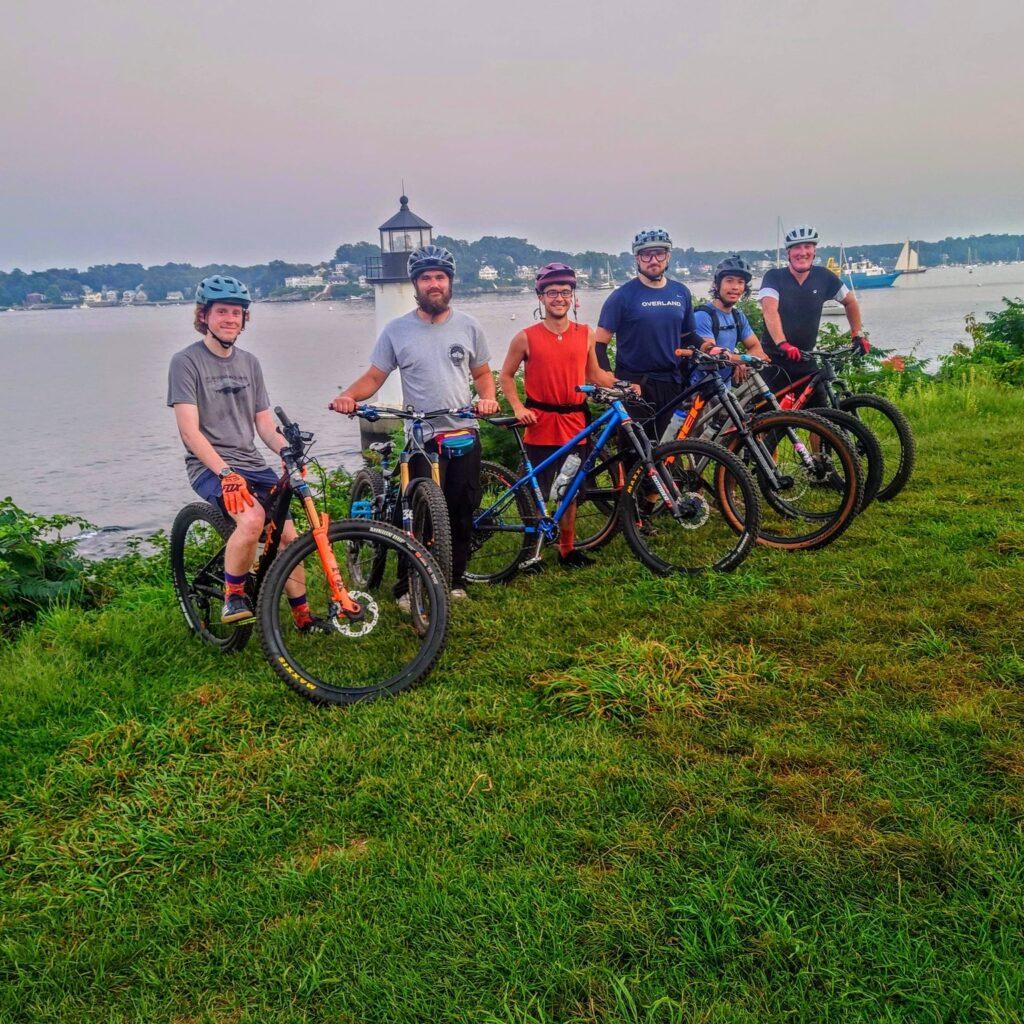 A group of mountain bikers posing in front of a body of water on Small Business Saturday.