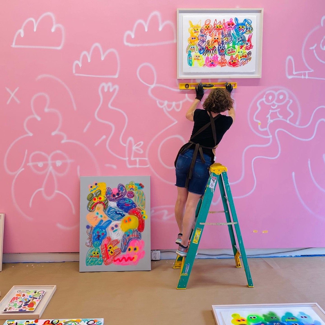 A woman on a ladder painting on a pink wall.