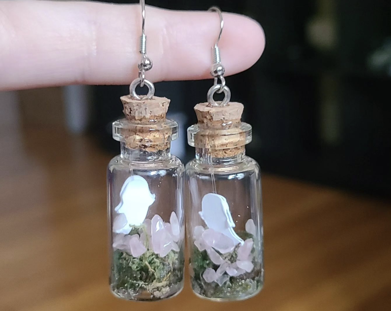 A person is holding a pair of glass bottle earrings.