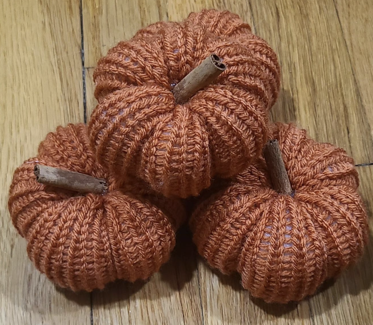 Three knitted pumpkins on a wooden floor.