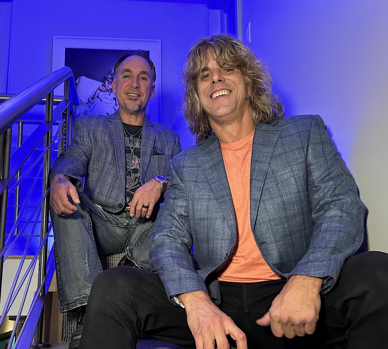 Two men sitting on stairs in a blue room.