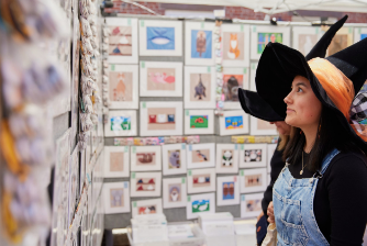 A lady sporting a mystical wizard hat is engrossed in examining photos displayed on a wall.