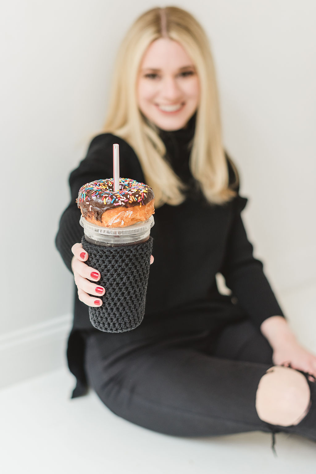 A woman with blonde hair is comfortably settled on the floor, lovingly cradling a cup shaped like a donut.