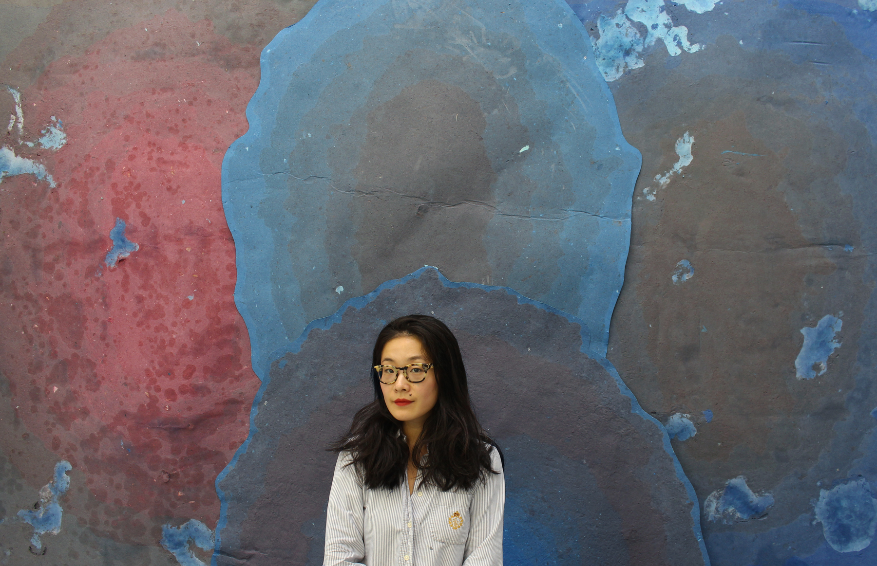 A woman stands before a painting displaying various shades of blue.