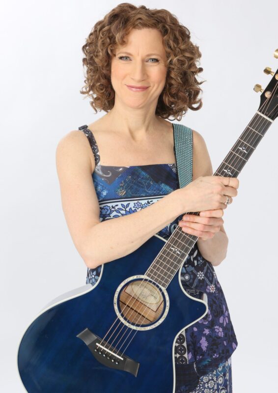 A lady with spiraled hair cradles a sky-blue acoustic guitar.