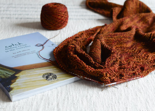 A cozy knitted scarf and an engaging book placed invitingly on a bed.