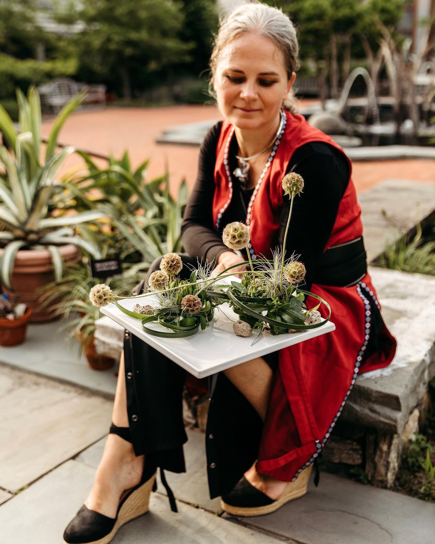 A lady outdoors, gracefully holding a tray filled with potted plants.