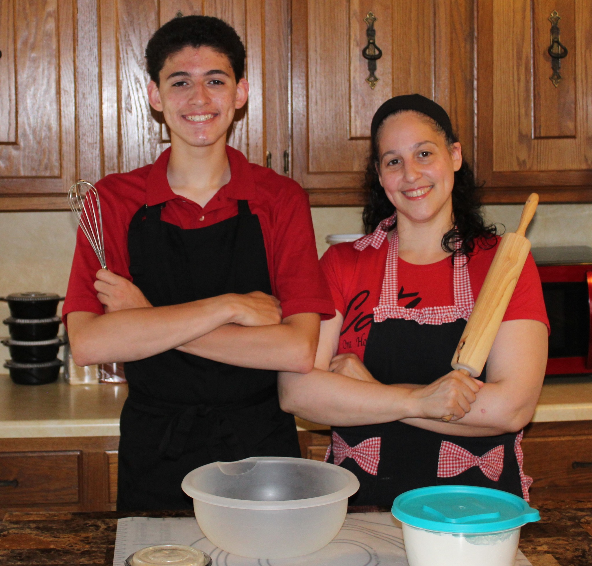 A happy woman holding a rolling pin and a young man armed with a whisk, stand in the kitchen, eager to start cooking or baking.