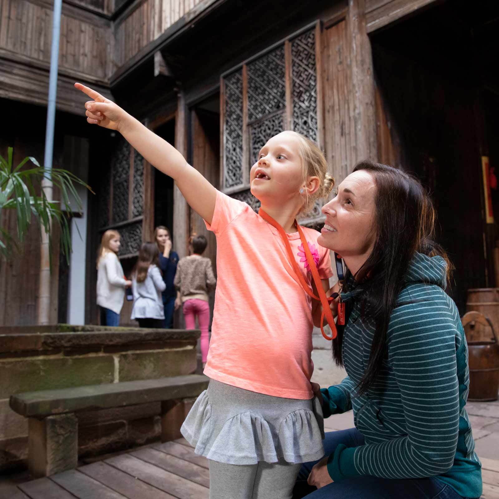 A young kid showing her engaged mom something fascinating during their family outing at a classic courtyard.