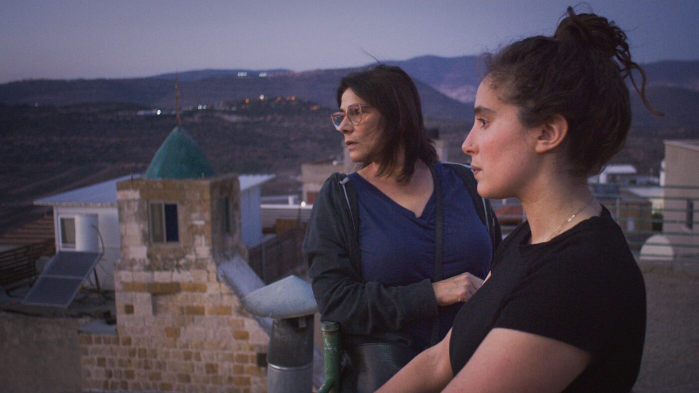 Two ladies on a balcony viewing a scene at twilight.