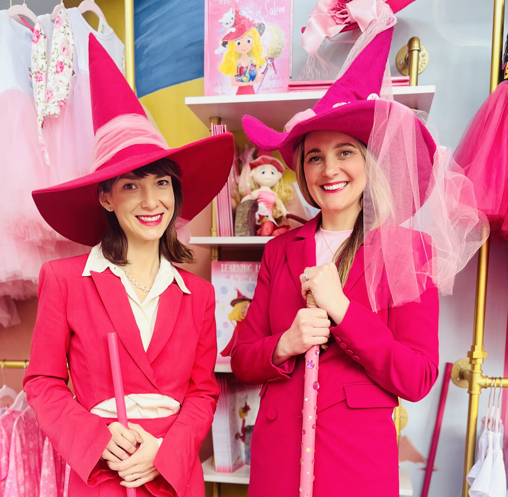 Two joy-filled people donning bright pink wizard outfits featuring pointed hats, complete with wands in hand.