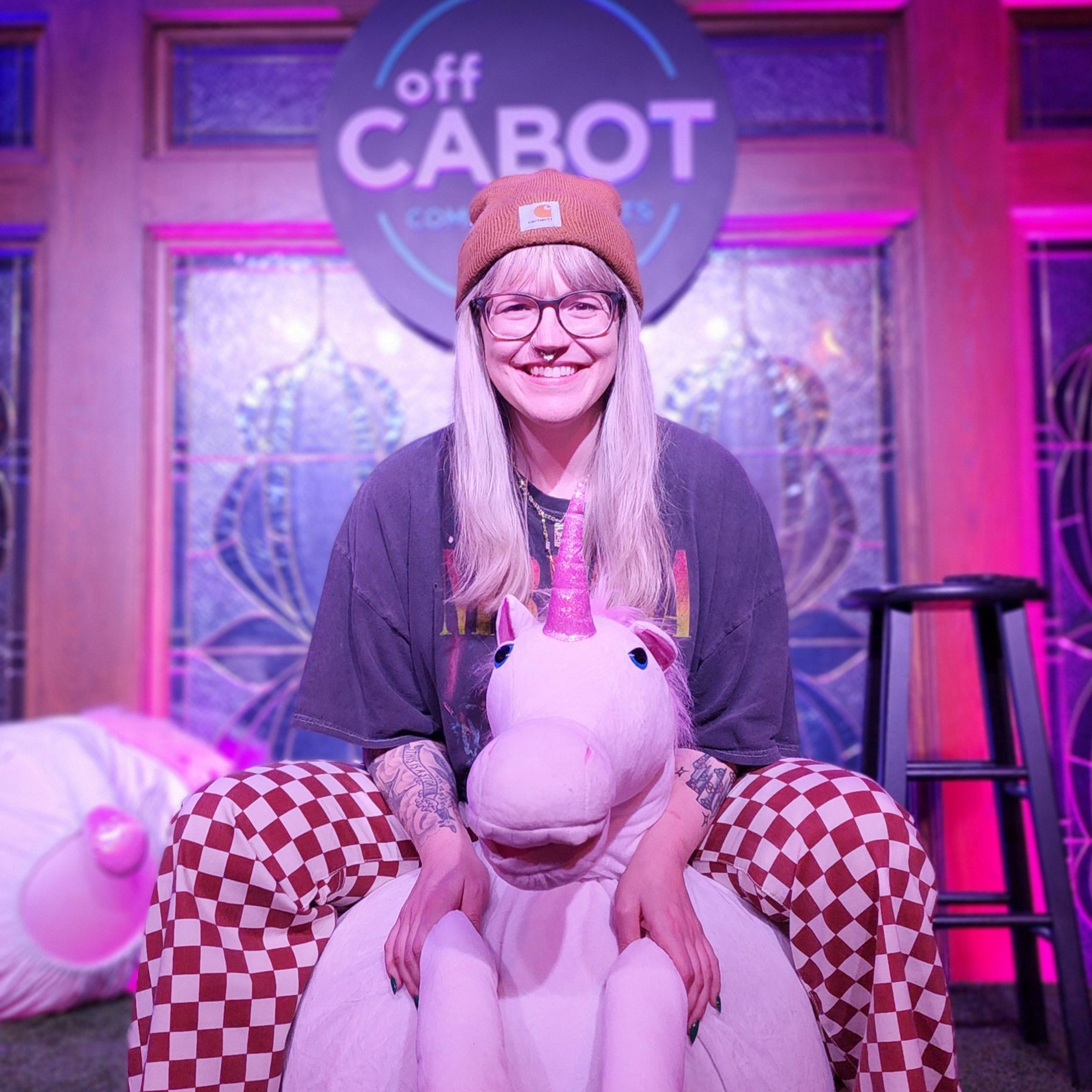 A cheerful woman sitting comfortably on a fluffy unicorn chair, surrounded by a room illuminated with soft purple light.