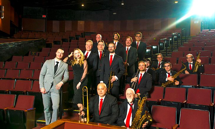 Band of artists grouped together for a photo in a theater venue.