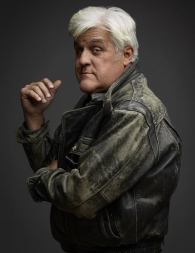 An older gentleman with snow-white hair sports a stylish leather jacket, exuding confidence in his pose. He casts an over-the-shoulder glance at the camera.