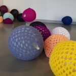 A variety of handcrafted, colorful crochet balls showcased on a gallery floor, perfect for enhancing your living space.