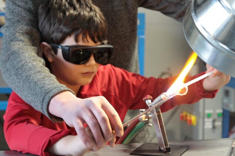 A kid dons protective goggles while using a blowtorch to heat materials during an engaging hand-on workshop experience.