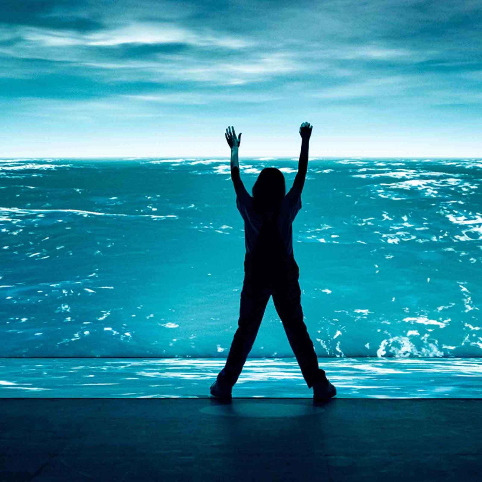 A person's silhouette is seen with hands up, set against a vivid blue, digitally crafted ocean background.