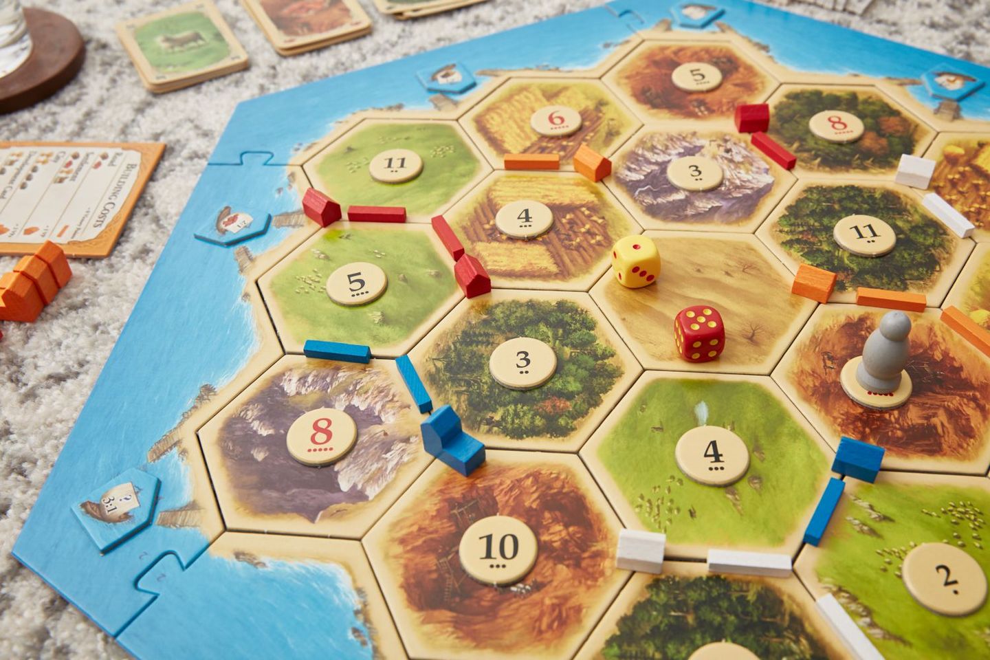 A detailed snapshot of a Settlers of Catan game in progress, showcasing varied resource tiles, numbered chits, dice and color-coordinated player settlements.