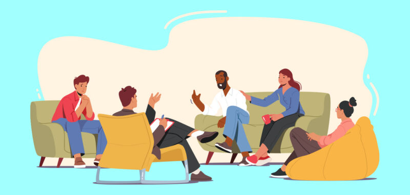 Five individuals from various backgrounds participate in a laid-back conversation. They comfortably sit on sofas and a bean bag, creating an informal indoor environment.