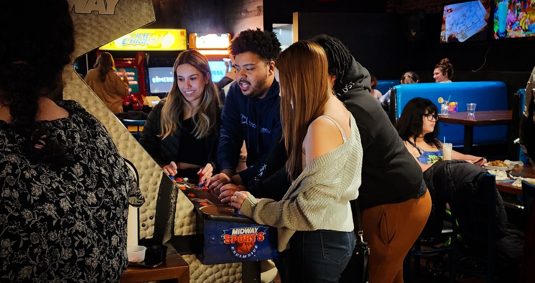Friends gathering to explore menu options at an exciting arcade, with visuals of fun arcade games in the backdrop.