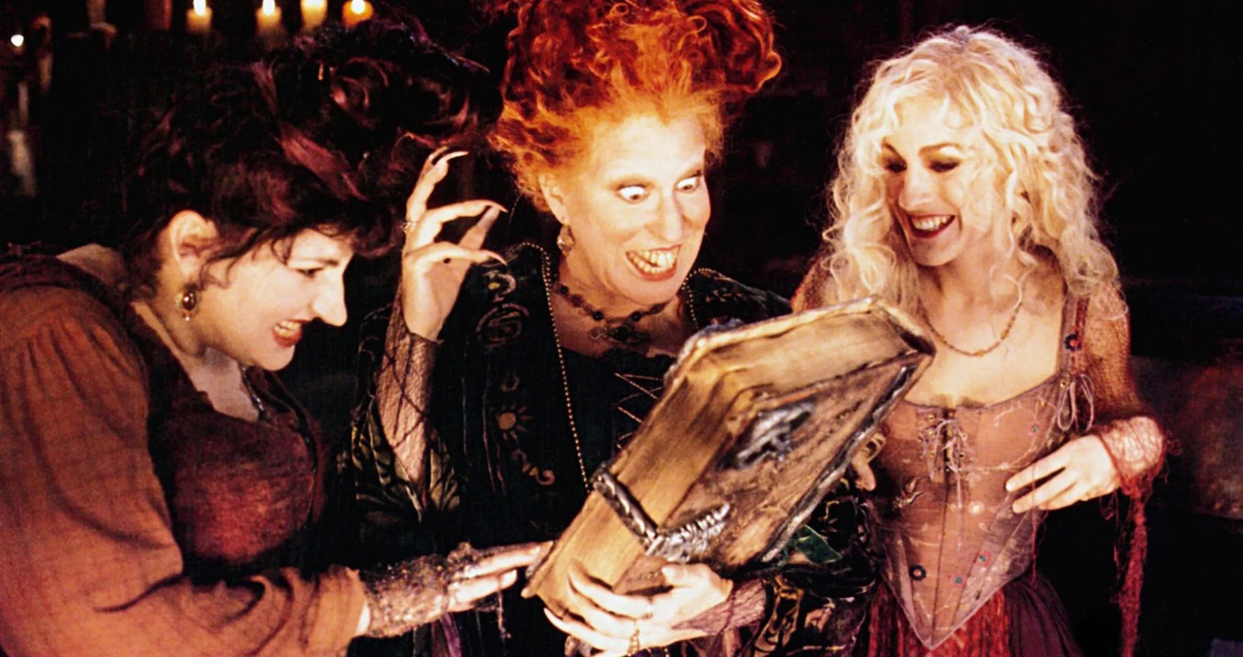 Three women, styled as mystical witches, show visible excitement and curiosity. One reads from a large book in an enthralling environment with dim lighting.