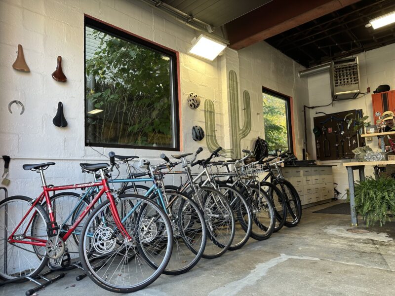 A variety of bikes are neatly arranged in a brightly lit bike store, where bicycle accessories and components adorn the walls.