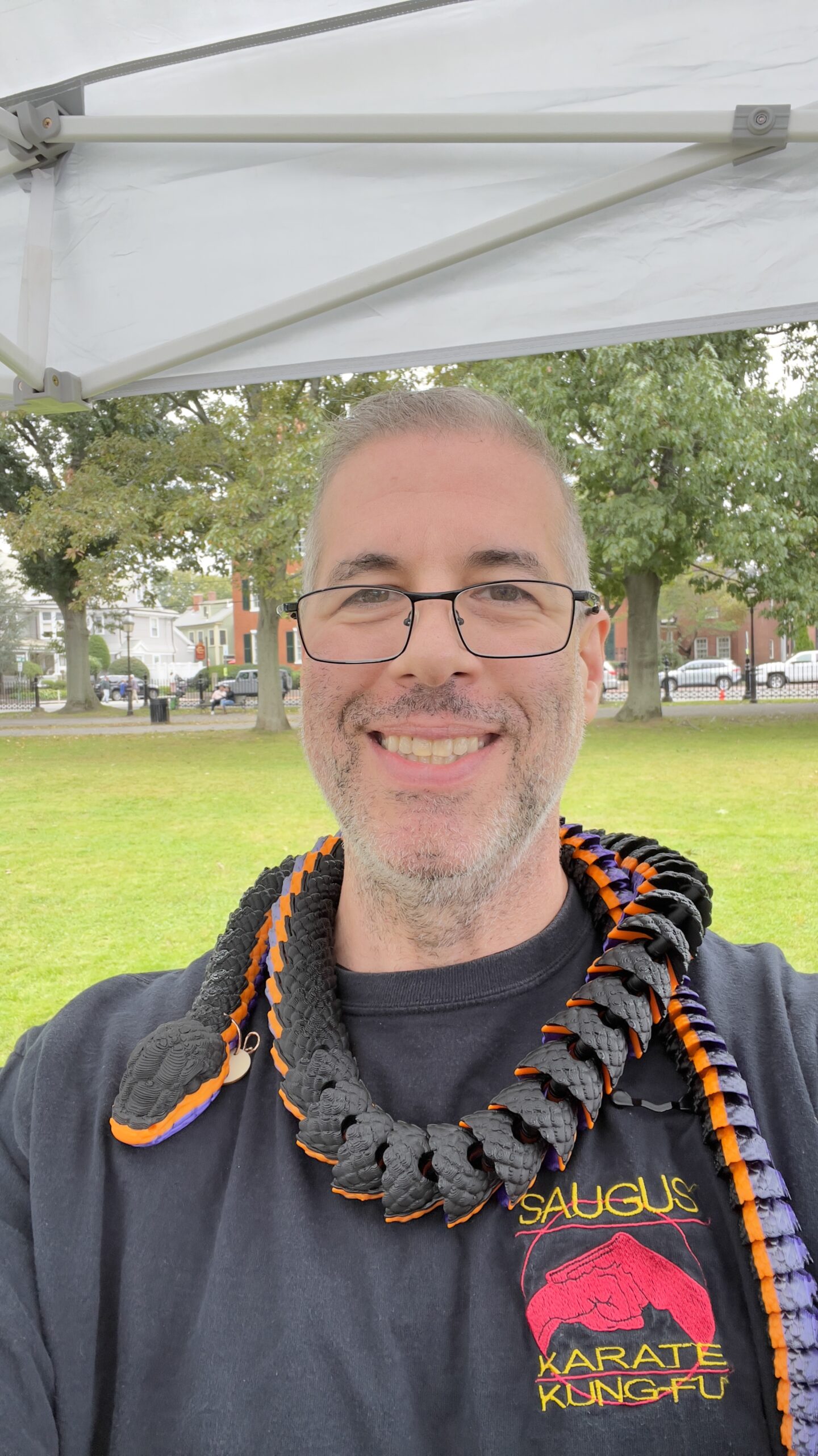 Member Spotlight: Thistle Art - Picture a radiant man with glasses, proudly wearing his martial arts inspired t-shirt. He dons a ceremonial rope around his neck, adding an attractive touch to his outfit. All this while standing outdoors under a pristine white canopy.