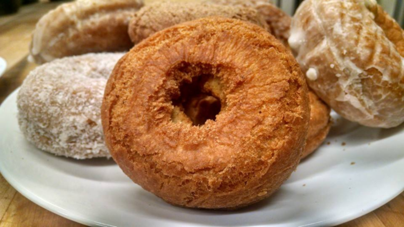 Picture this: a wooden table showcasing a tempting plate of assorted donuts. Up front, there's a classic plain cake donut, while others boast powdered sugar and glossy glaze.