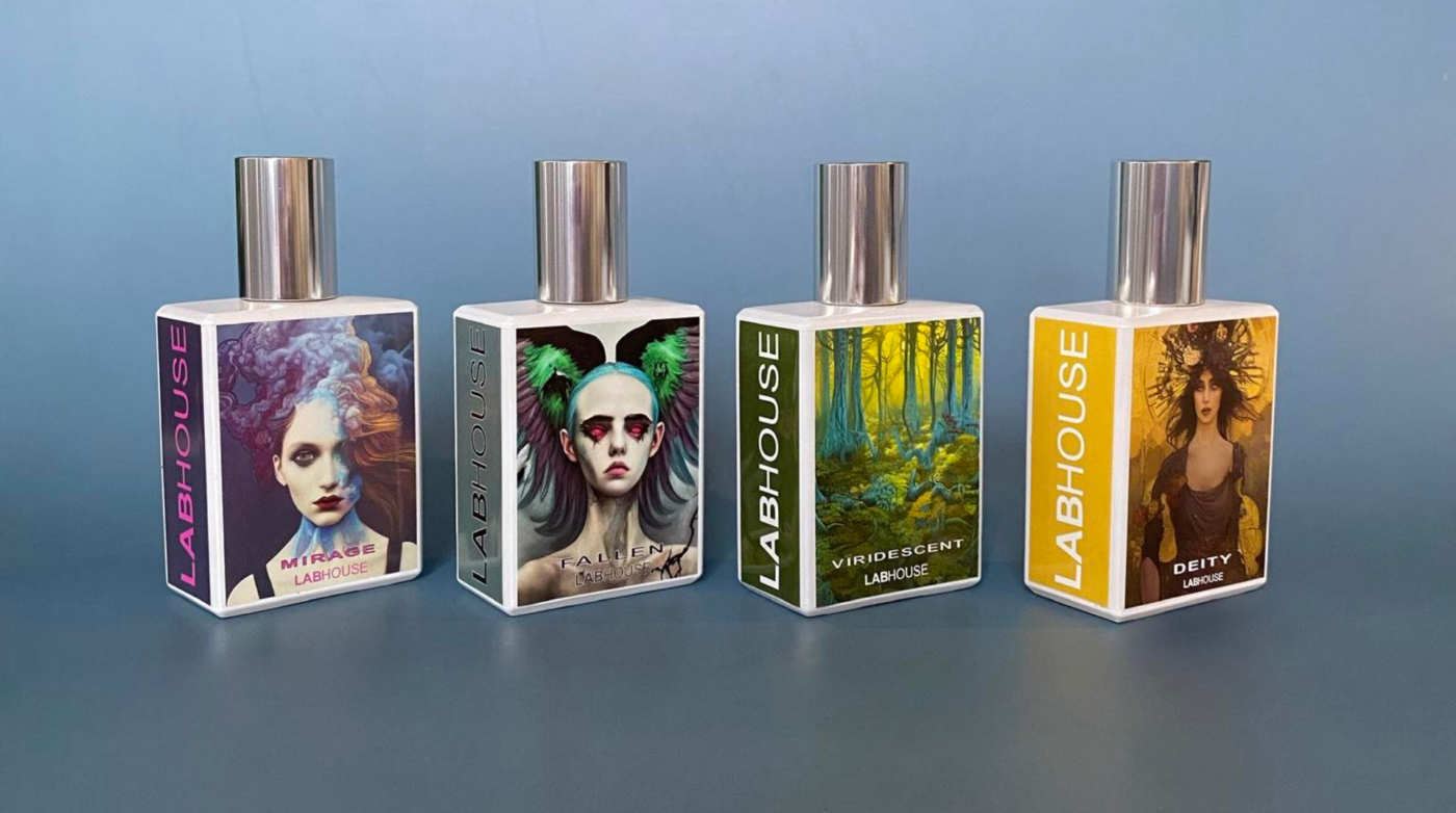 Four perfume bottles—Mirage, Fable, Viridescent, and Deity—each showcasing unique artistic label designs, lined up against a blue backdrop.