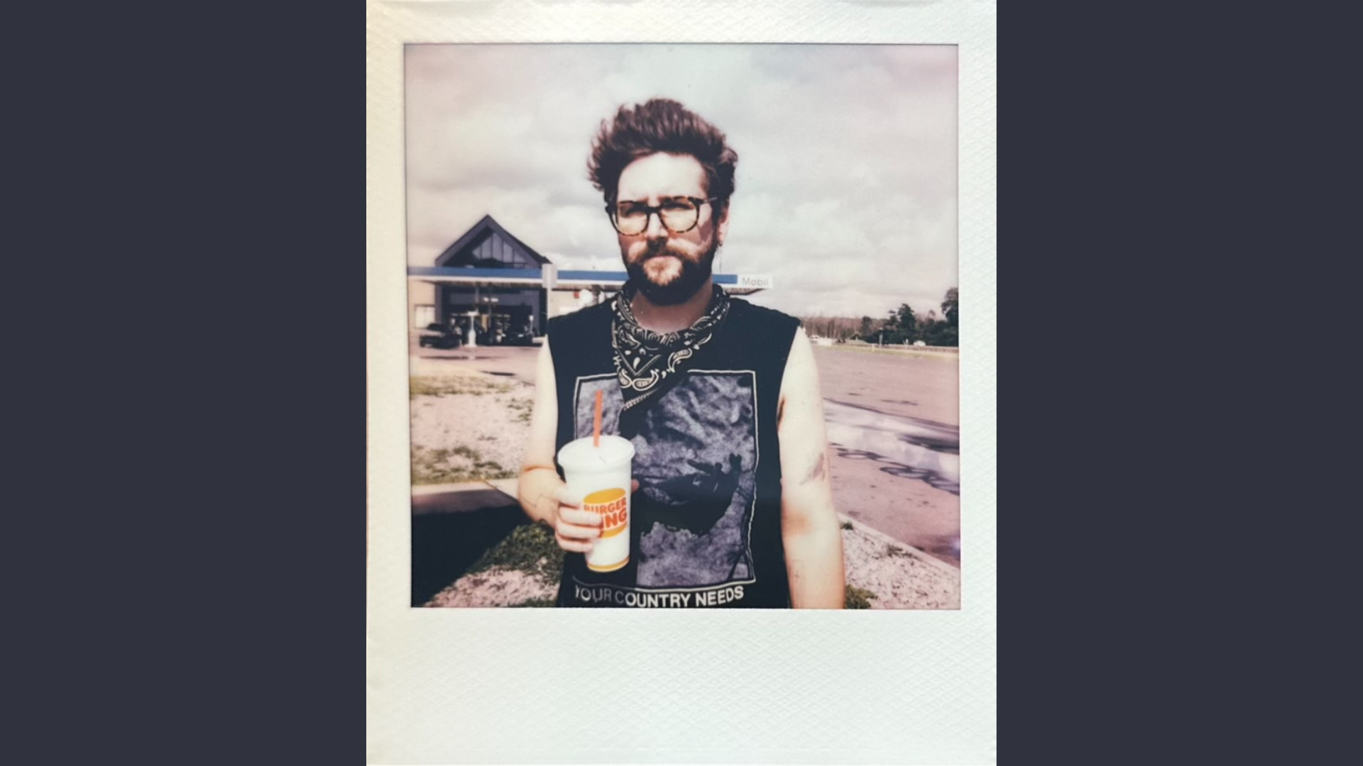 Check out our featured member: A bearded, glasses-wearing enthusiast savoring a drink in the lively outdoors. They're positioned near a bustling street, highlighted by the iconic glow of Witch City Wicks in the background.