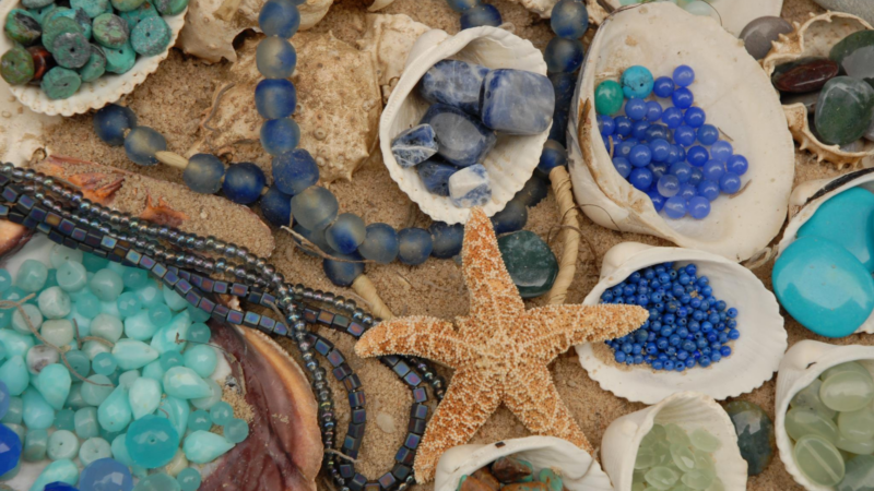 Discover the beauty of assorted blue beads and stones nestled within seashells on sandy shores, all highlighted by a striking central starfish. Perfect for beach-inspired crafts or decor, these ocean treasures bring a coastal charm to any project. Dive into seaside inspiration!