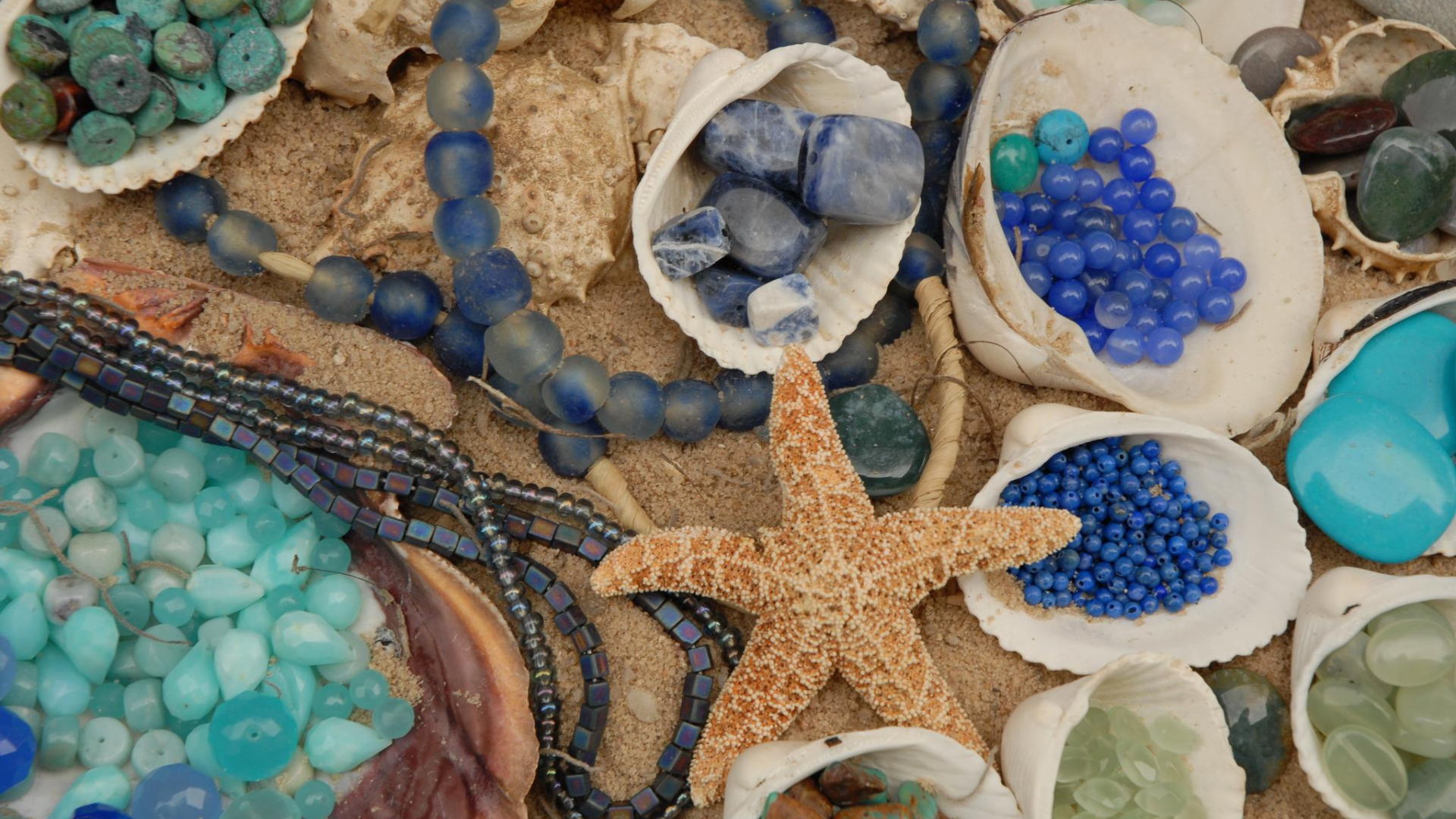 Discover the beauty of assorted blue beads and stones nestled within seashells on sandy shores, all highlighted by a striking central starfish. Perfect for beach-inspired crafts or decor, these ocean treasures bring a coastal charm to any project. Dive into seaside inspiration!