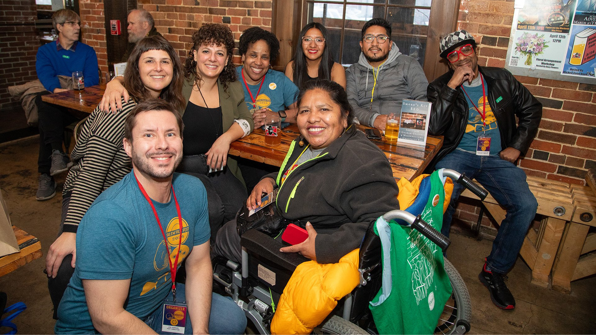 Nine smiling people, including one using a wheelchair, gather around a restaurant table—Essex County’s vibrant community spirit shines.