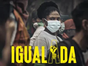 In a vibrant image, a woman is seen wearing a face mask amidst a bustling crowd. The word **IGUALADA** stands out boldly in bright yellow, capturing immediate attention.