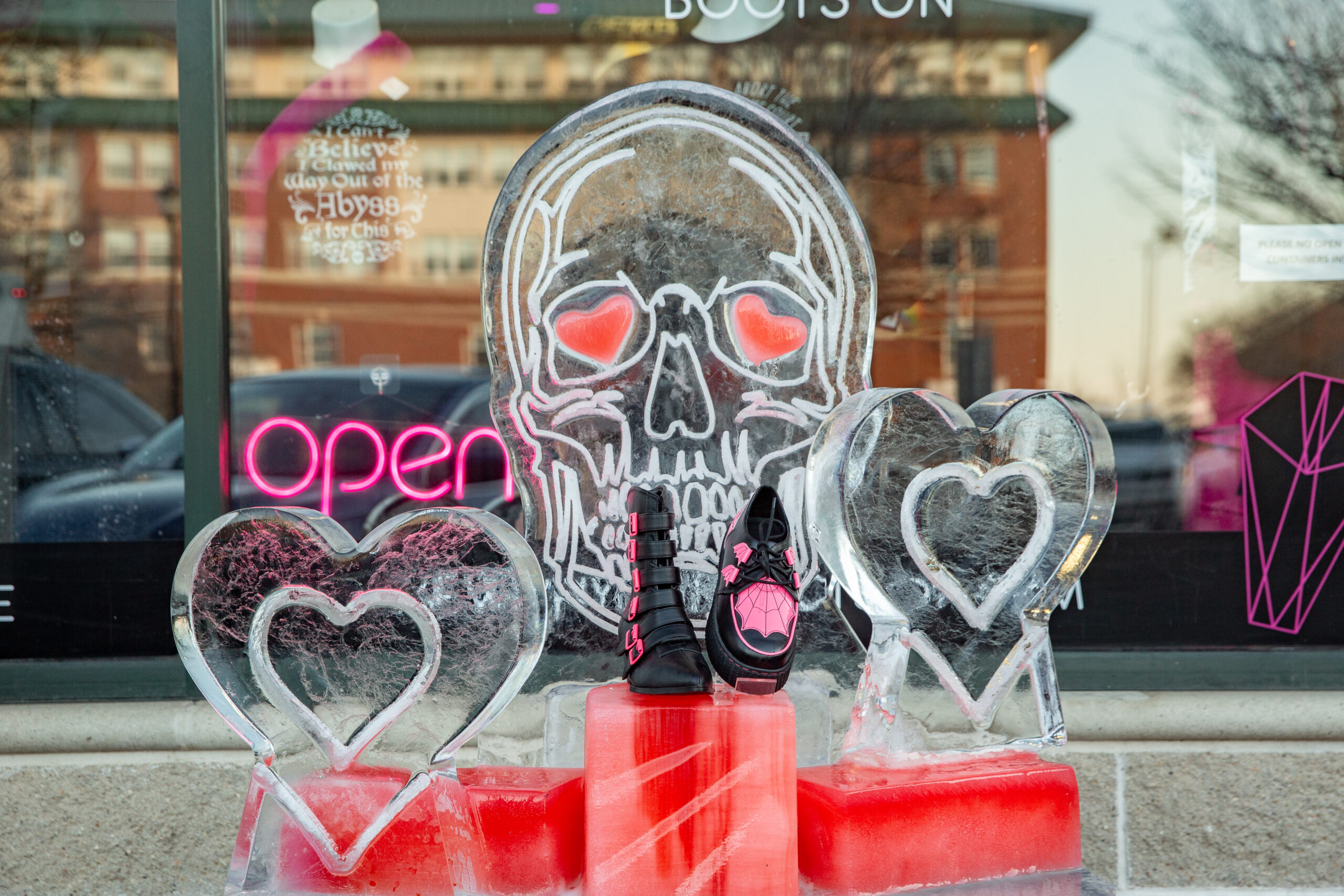 Check out our eye-catching display: stunning ice sculptures of a skull and two hearts, all set on striking red pedestals right in front of our store window. Don't miss the vibrant neon "open" sign inviting you to explore more inside!.
