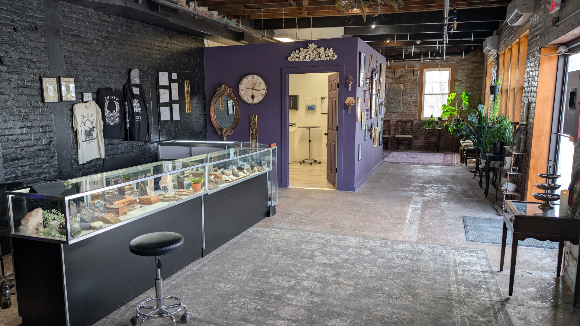 Transform your store into a customer magnet with these design tips: Install a glass display case to highlight your best products, drawing in shoppers like moths to a flame. Pair it with a striking purple accent wall featuring an eye-catching clock and art pieces for visual intrigue. Introduce greenery with potted plants to create a welcoming atmosphere, complemented by the warm tones of wooden flooring underfoot. Your store will not only look inviting but also encourage customers to linger, explore, and shop.