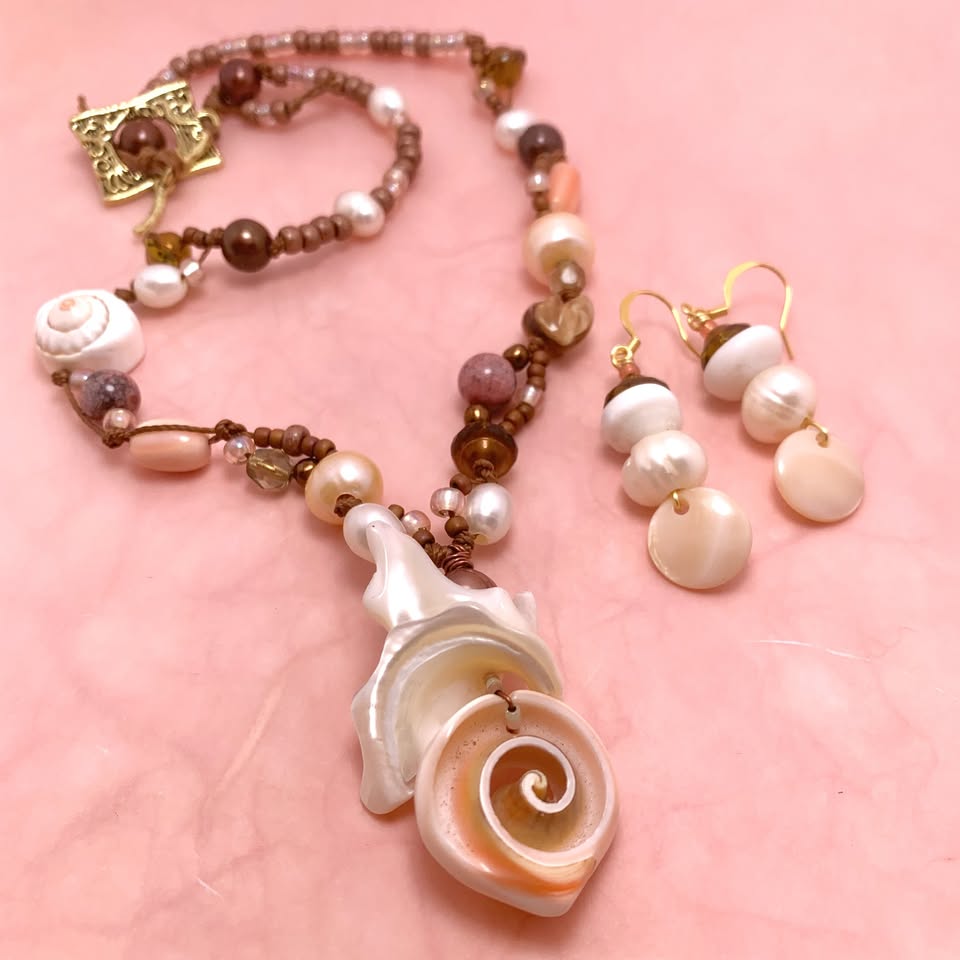 Discover our stunning jewelry set, featuring a necklace and earrings adorned with charming seashell designs, lustrous pearls, and earthy brown beads. Perfectly displayed against a soft pink background for an elevated presentation.