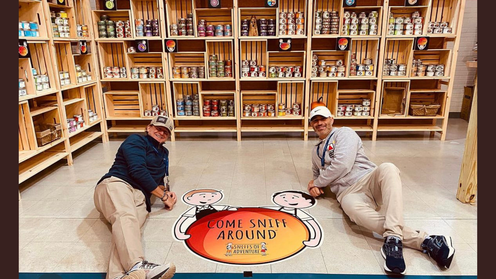 Discover a vibrant world of creativity and fragrance: Two people, sporting caps and jackets, are seated on the floor in front of shelves filled with colorful jars. Between them, a floor decal reads "Meet the Member: Lory Sun Artistry," inviting you to dive into their remarkable artistry.