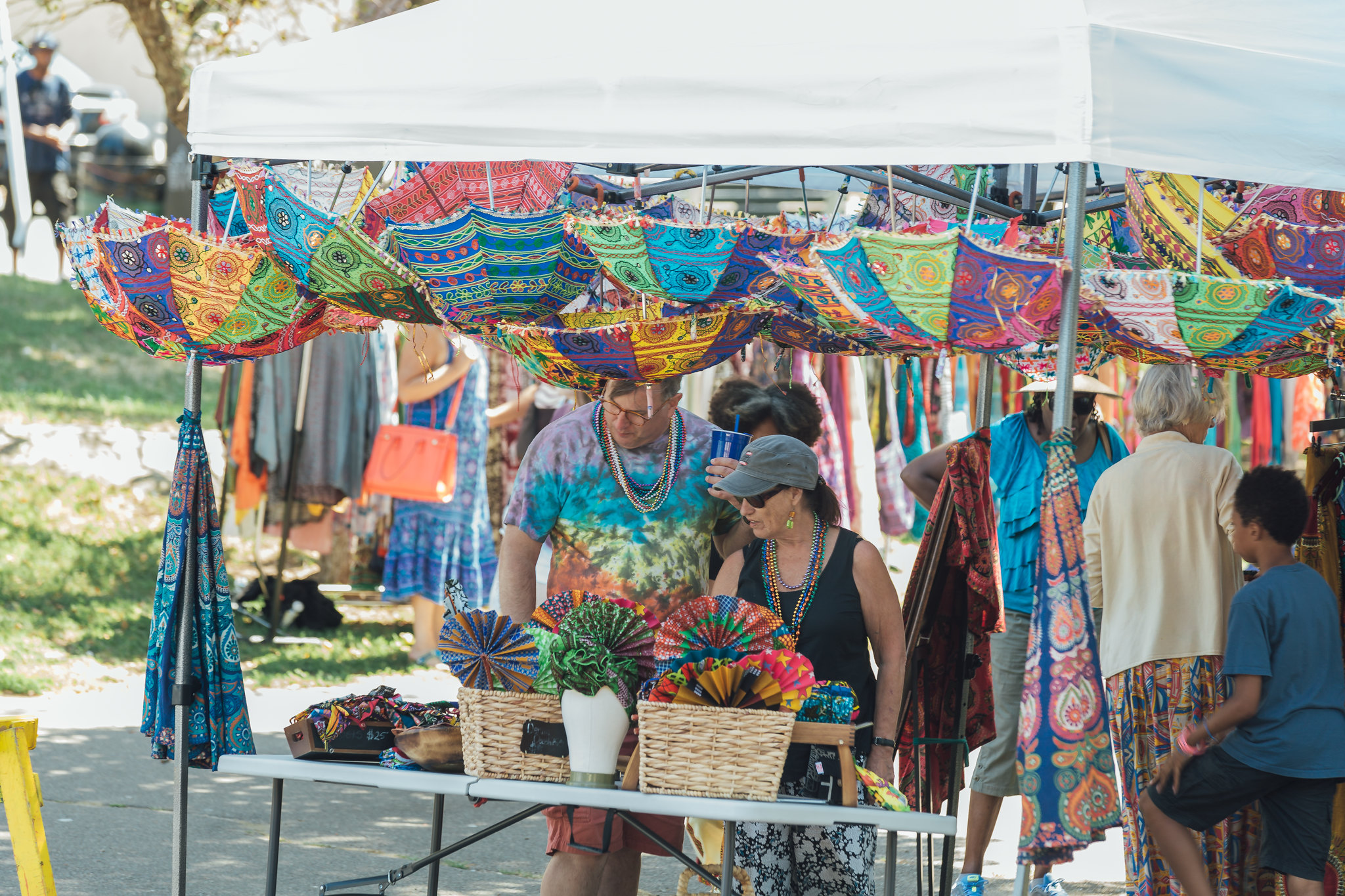 Explore a vibrant market stall featuring an array of colorful umbrellas and fans. Shoppers wander under a pristine white canopy, drawn to these eye-catching items that blend style with functionality.