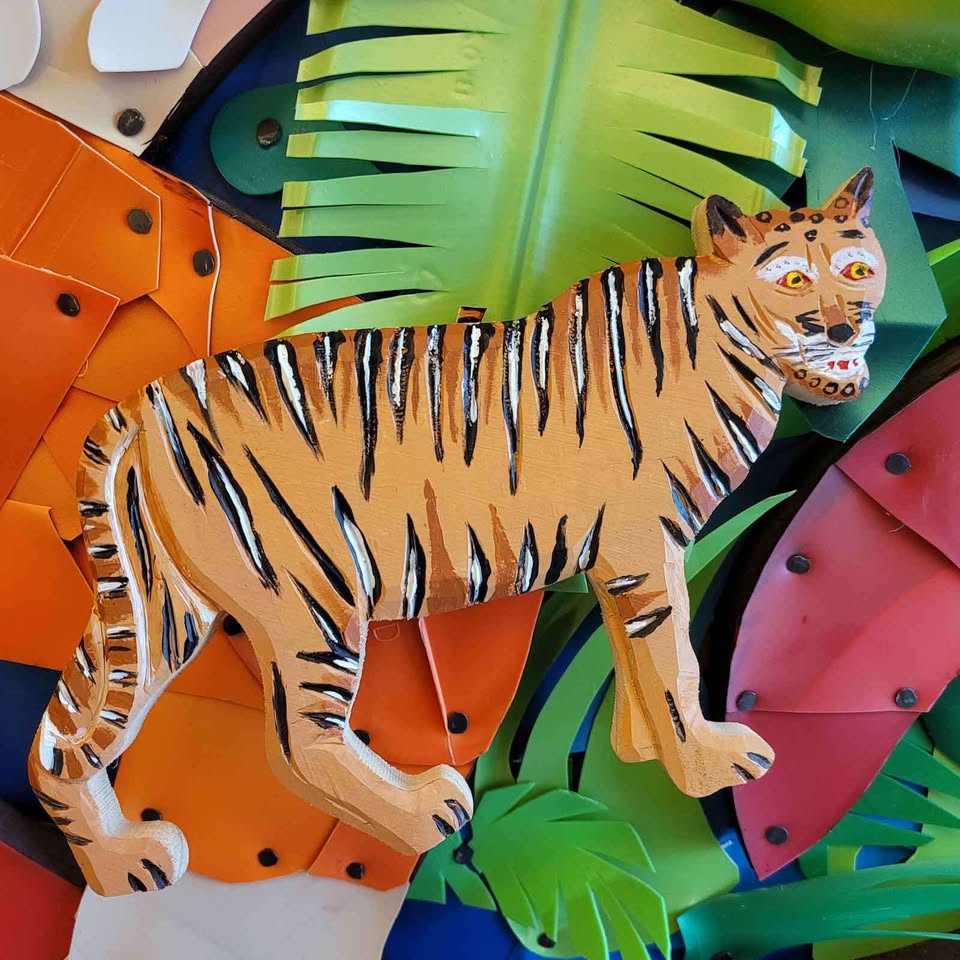 Meet a striking, playful tiger brought to life in bold colors and textured cut-out materials. Set against a lively backdrop of layered leaves and dynamic abstract shapes, this eye-catching tiger pops with contrasting black stripes and a charming cartoon grin—an instant standout for anyone drawn to creative, art-inspired designs.