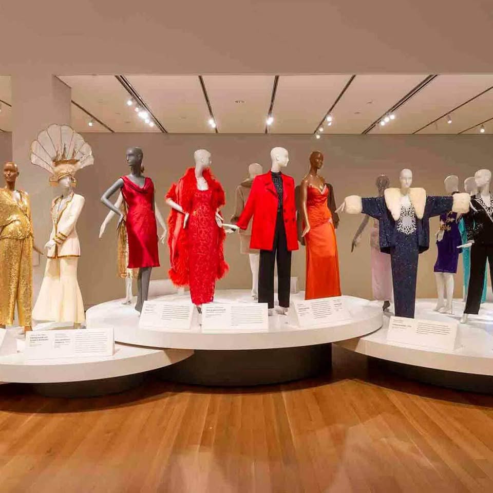 Step into a fashion wonderland where chic mannequins model an array of colorful formal wear, from elegant dresses to stylish suits. Vibrant hues and diverse styles come to life in a museum-like setting against a backdrop of rich wooden floors, offering a captivating experience for fashion enthusiasts.