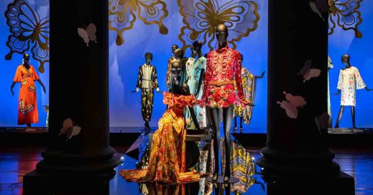 Absolutely! Here’s a more dynamic, community-focused alt text for your image: Mannequins in bold, butterfly-inspired outfits shine before our blue and gold butterfly backdrop—celebrating local style and creativity.