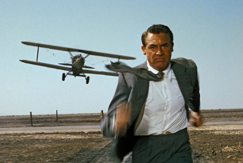 A man in a suit sprints across an open field as a vintage crop-duster buzzes low behind him under bright, clear skies—capturing our creative drive and bold spirit.