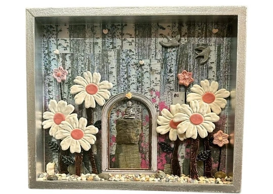 A lively shadow box blooms with white-pink daisies, joyful birds, and hearts—our creative community shines amid birch trees and pebbles.