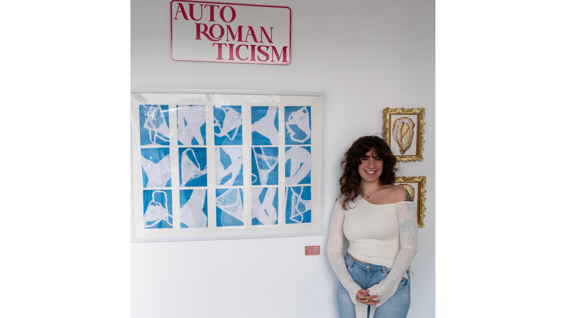 Smiling beside bold, blue artwork and “AUTO ROMANTICISM” sign, our vibrant member lights up our creative community wall.