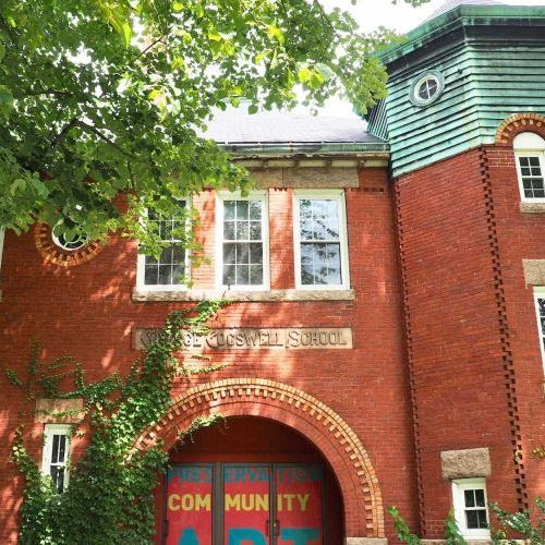 Absolutely! Here’s a revised alt text that’s concise, vibrant, and community-focused: Our historic red-brick school bursts with ivy, colorful 'ART' doors, and creative spirit—where our community connects and thrives. Let me know if you have any specific events or local artists to highlight in the image for even more tailored alt text!.